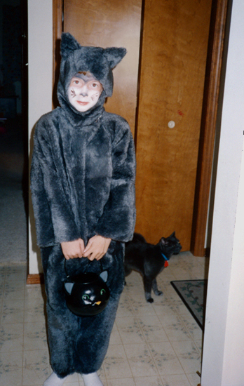 Child in gray cat costume for Halloween, real gray cat in background
